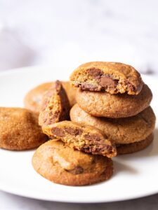 eggless chocolate chip cookies stacked with some halved cookies on a white plate