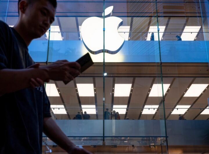 A pedestrian uses a smartphone while walking past an Apple store and logo in Hong Kong.