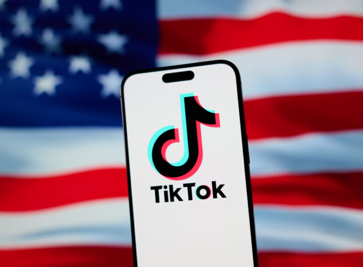 The TikTok app and logo are seen on a mobile device in front of a US flag